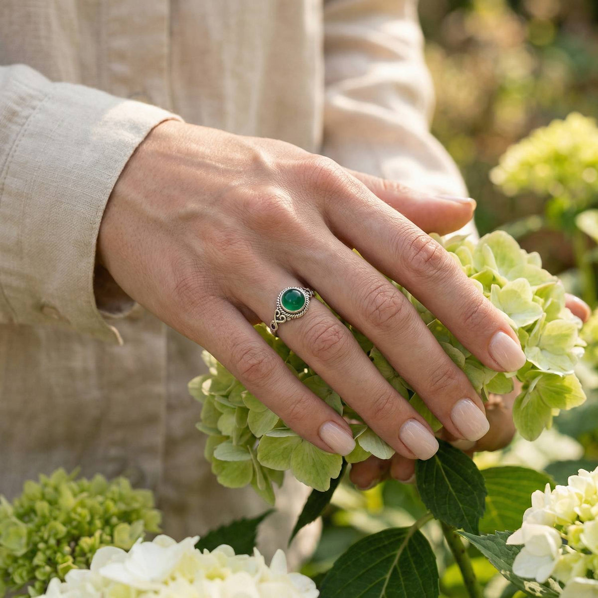 Silberring mit grüner Onyx an der Hand zwischen Blumen