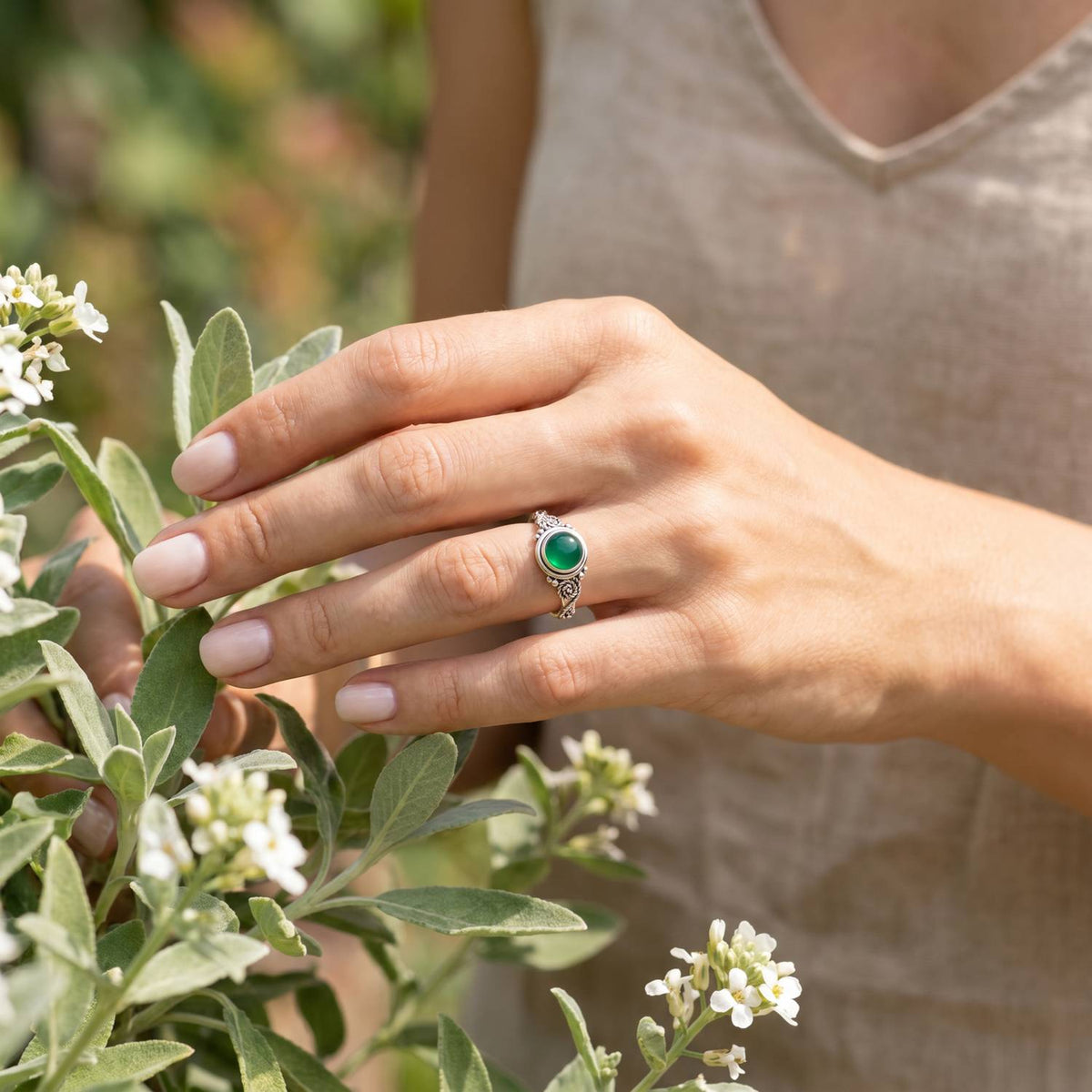 Silberring mit grüner Onyx an der Hand zwischen Blumen