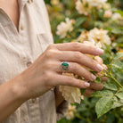 [KI] Silberring mit grüner Onyx an der Hand zwischen Blumen