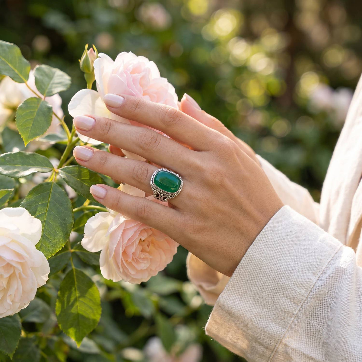 Silberring mit grüner Onyx an der Hand zwischen Blumen