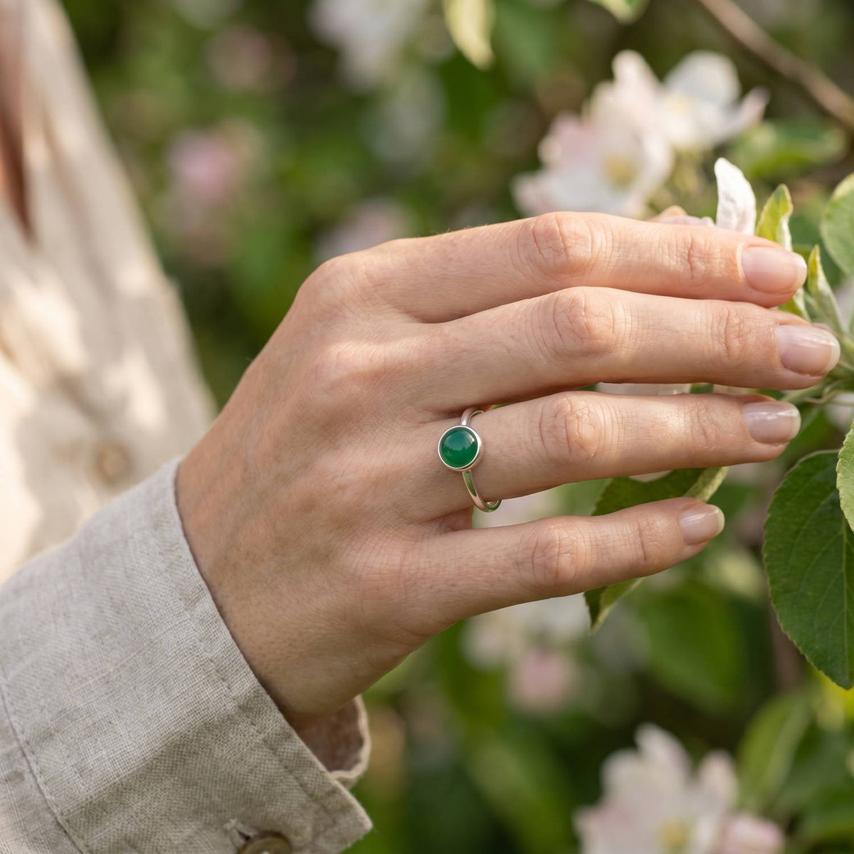 Silberring mit grüner Onyx an der Hand zwischen Blumen