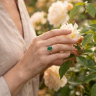 [KI] Silberring mit grüner Onyx an der Hand zwischen Blumen