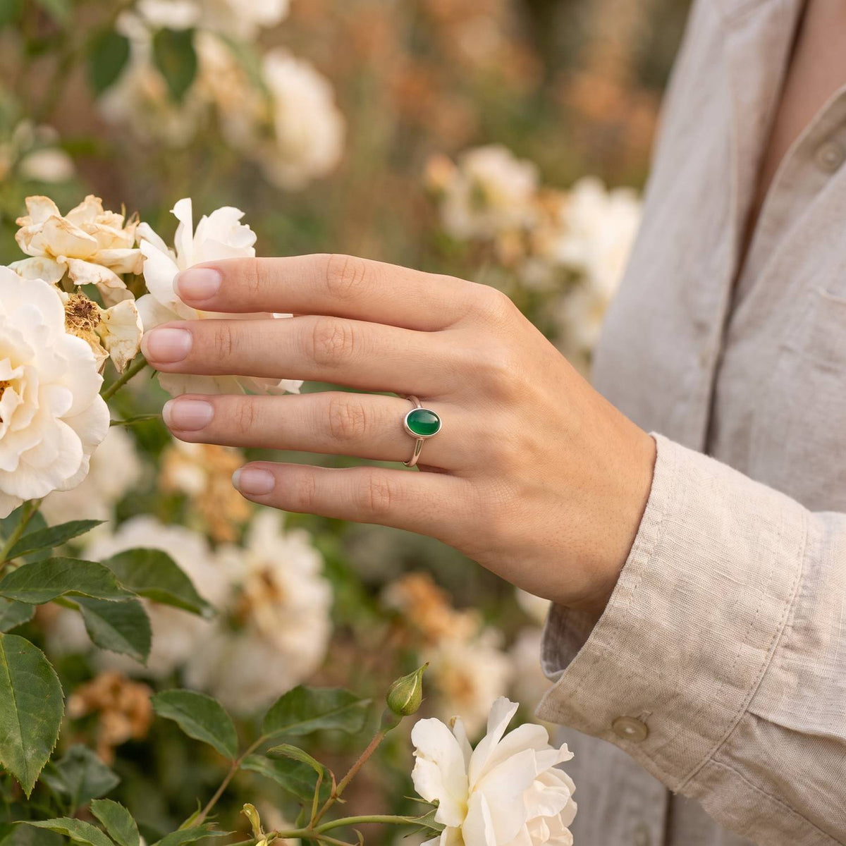 Silberring mit grüner Onyx an der Hand zwischen Blumen