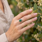 [KI] Silberring mit grüner Onyx an der Hand zwischen Blumen