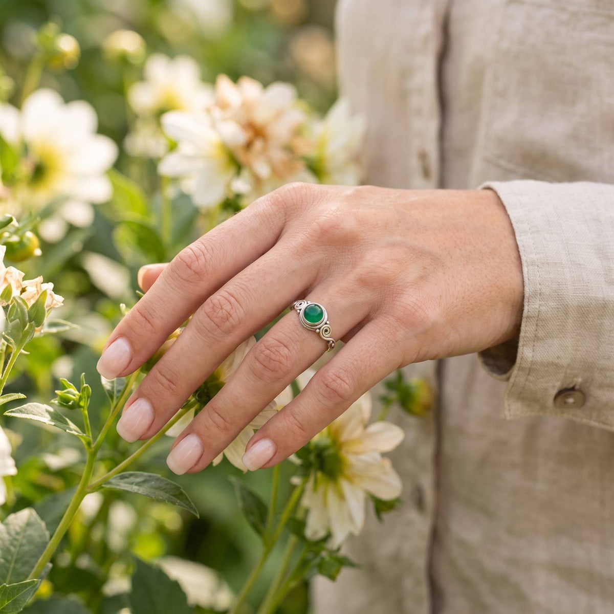 Silberring mit grüner Onyx an der Hand zwischen Blumen