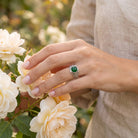 [KI] Silberring mit grüner Onyx an der Hand zwischen Blumen