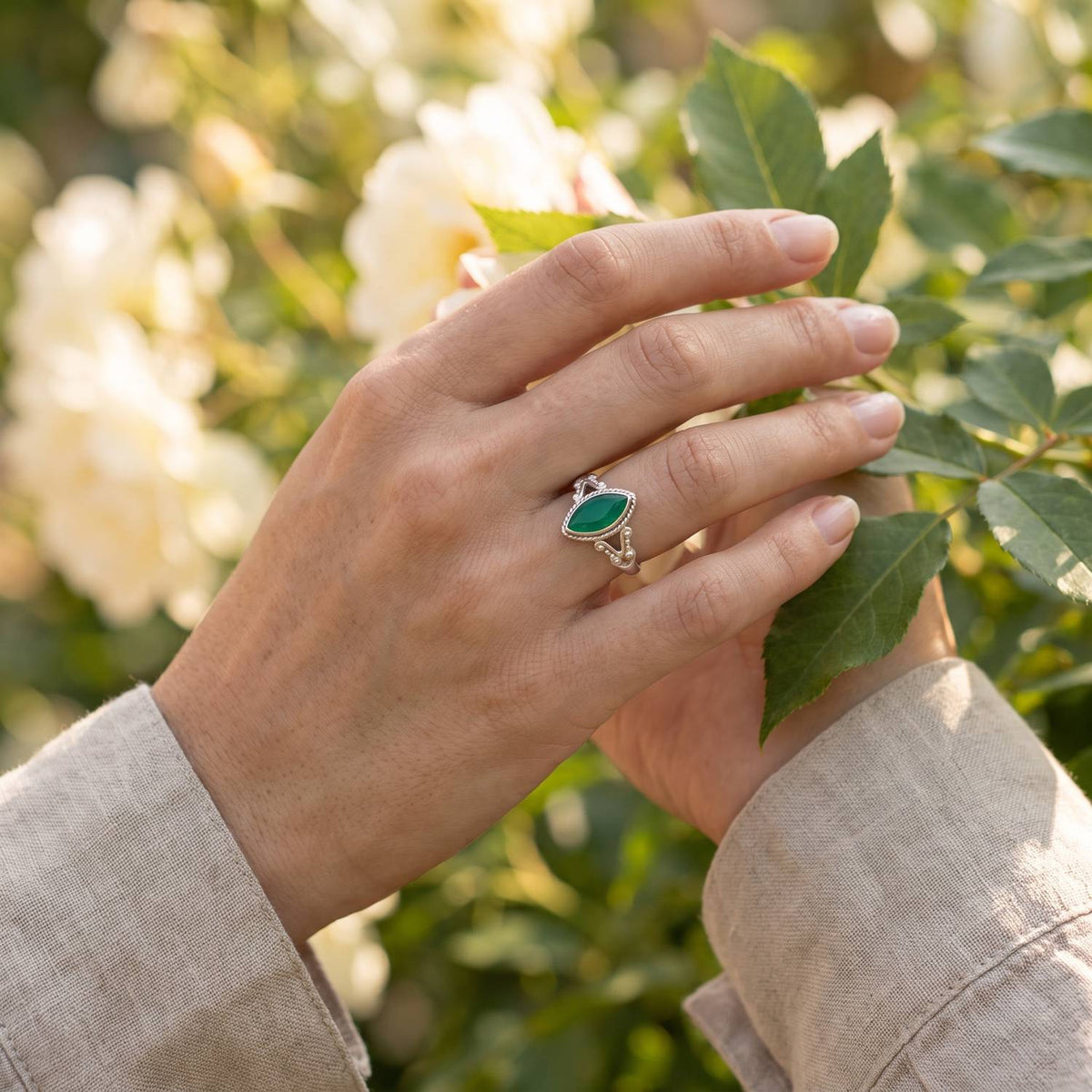 Silberring mit grüner Onyx an der Hand zwischen Blumen