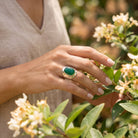 [KI] Silberring mit grüner Onyx an der Hand zwischen Blumen