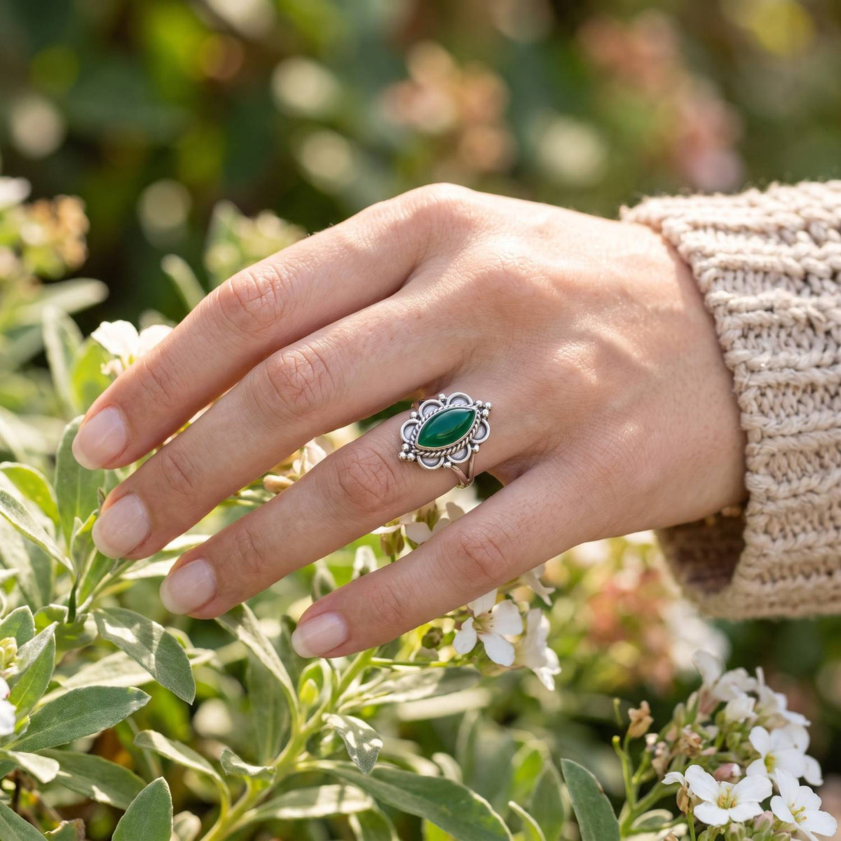 Silberring mit grüner Onyx an der Hand zwischen Blumen