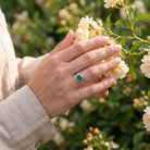 [KI] Silberring mit grüner Onyx an der Hand zwischen Blumen