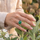[KI] Silberring mit grüner Onyx an der Hand zwischen Blumen