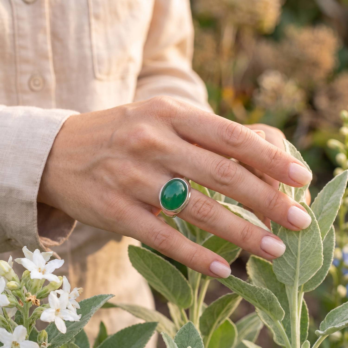 Silberring mit grüner Onyx an der Hand zwischen Blumen