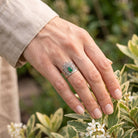 [KI] Silberring mit grüner Onyx an der Hand zwischen Blumen