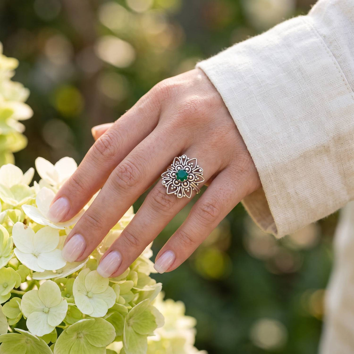Silberring mit grüner Onyx an der Hand zwischen Blumen