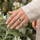 [KI] Silberring mit grüner Onyx an der Hand zwischen Blumen