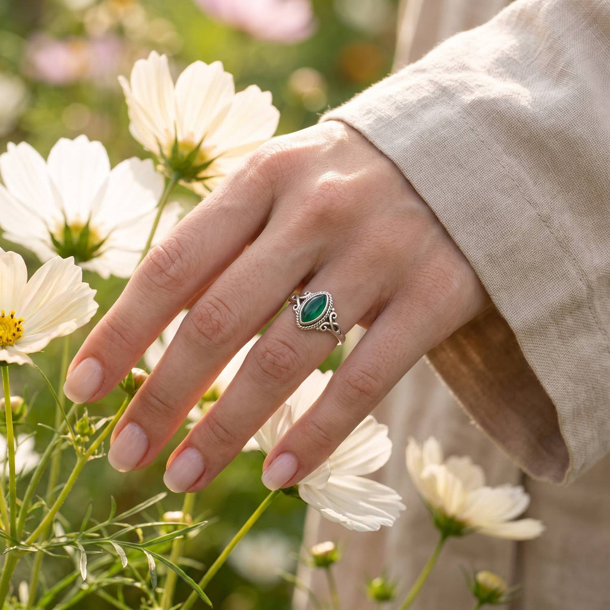 Silberring mit grüner Onyx an der Hand zwischen Blumen