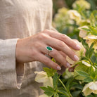 [KI] Silberring mit grüner Onyx an der Hand zwischen Blumen