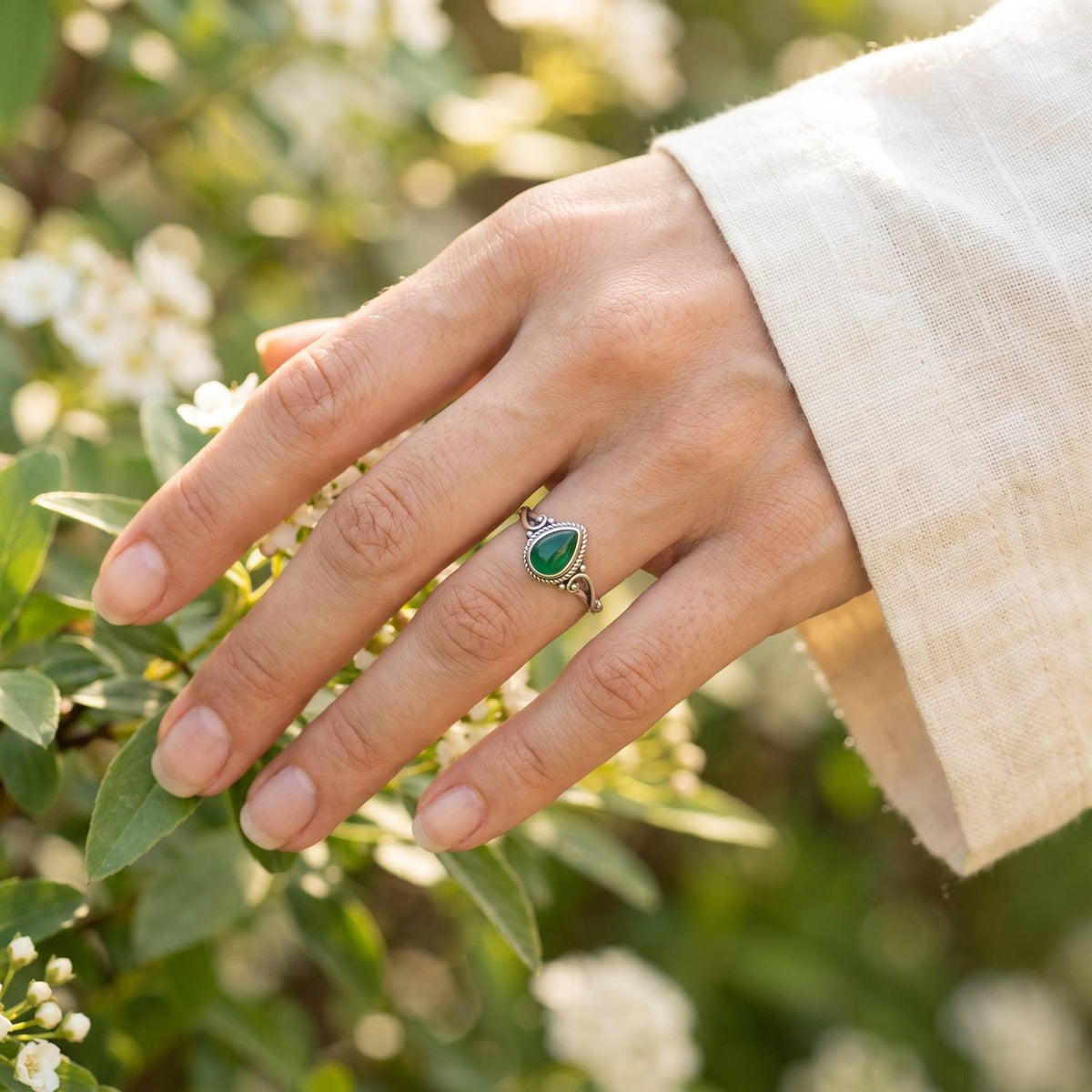 Silberring mit grüner Onyx an der Hand zwischen Blumen