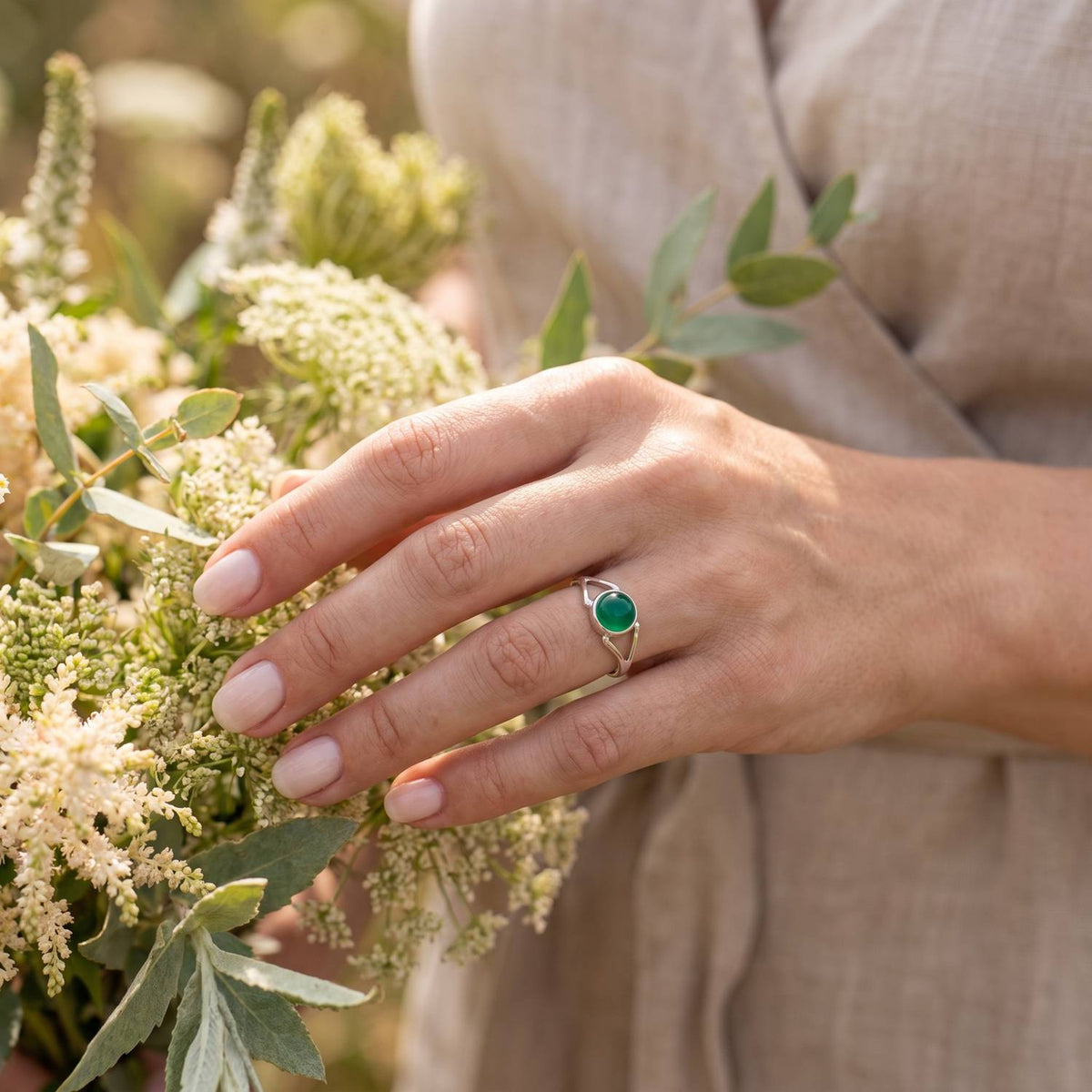 Silberring mit grüner Onyx an der Hand zwischen Blumen