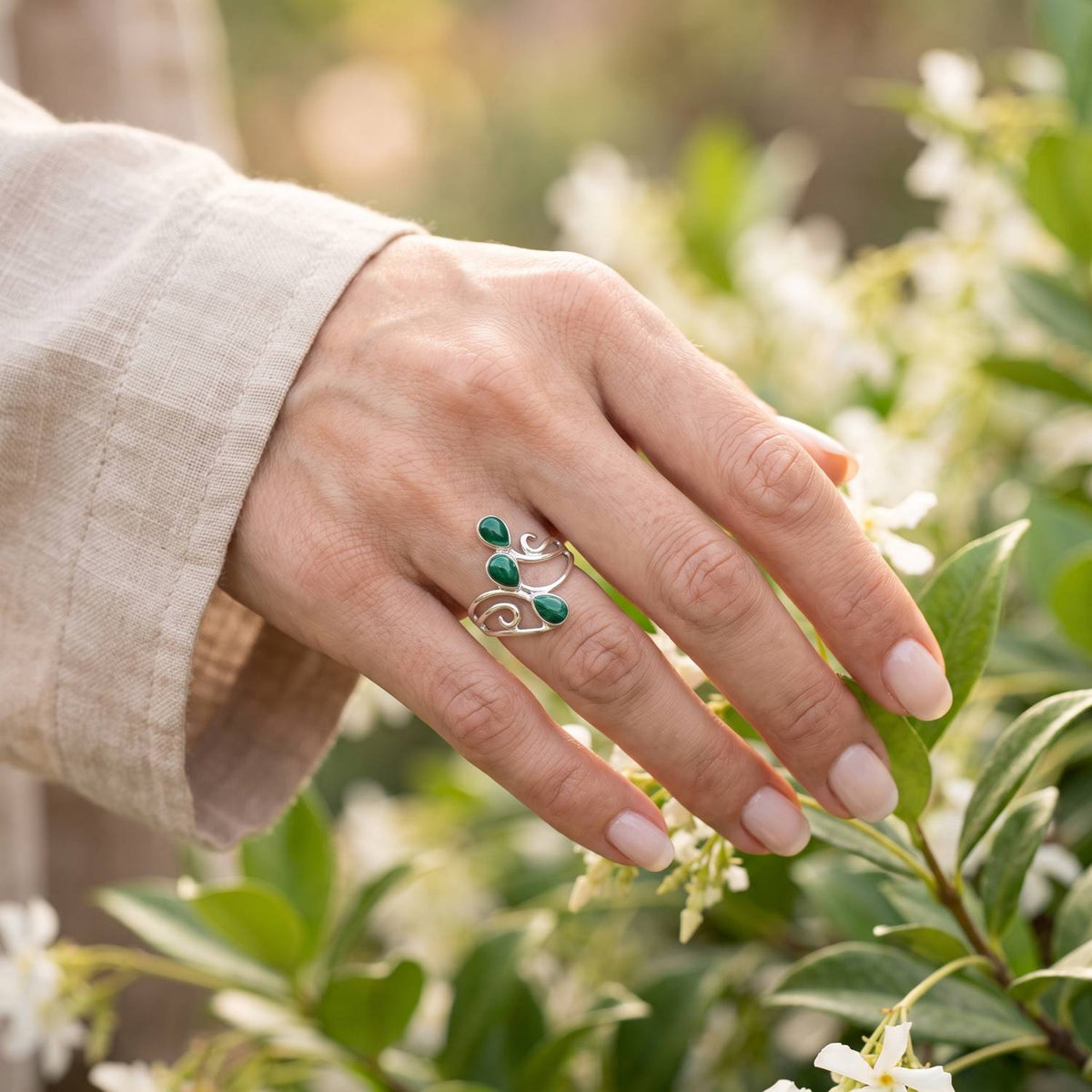 Silberring mit grüner Onyx an der Hand zwischen Blumen