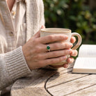 [KI] grüner Onyxring aus Silber getragen beim Lesen mit einer Tasse