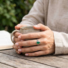 [KI] grüner Onyxring aus Silber getragen beim Lesen mit einer Tasse