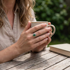 [KI] grüner Onyxring aus Silber getragen beim Lesen mit einer Tasse
